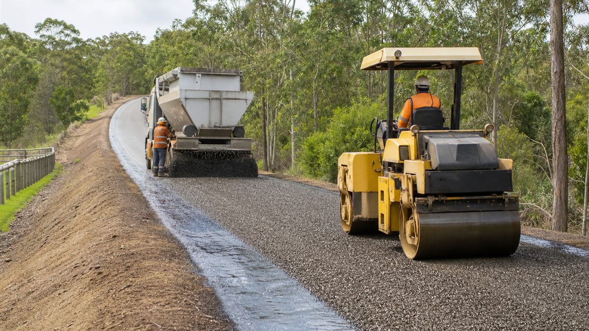 Road crew rolling aggregate into a freshly applied rural sprayed seal