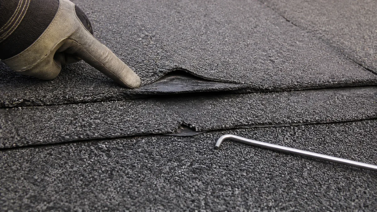 Gloved roof inspector indicating an open lap in granulated modified bitumen membrane
