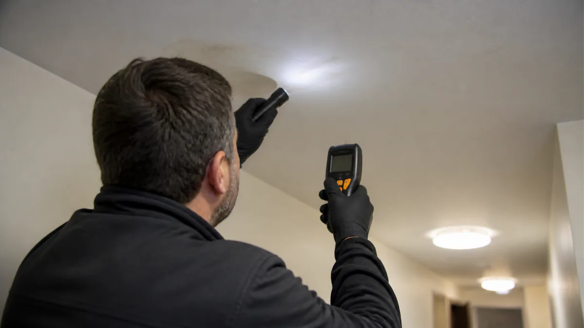 Building inspector examining a small ceiling water stain with a flashlight and moisture meter